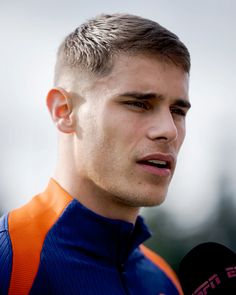 a close up of a person with a microphone in front of him and wearing an orange and blue shirt