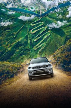 a jeep driving down a dirt road in front of a green mountain and sky filled with clouds