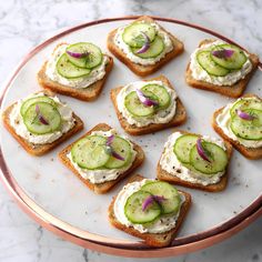 small sandwiches with cucumbers and cream cheese on them sitting on a white plate