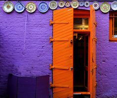 an orange door is open in front of a purple building with plates on the wall