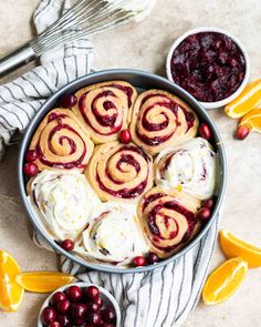 a pan filled with cranberry orange rolls next to lemons and whipped cream