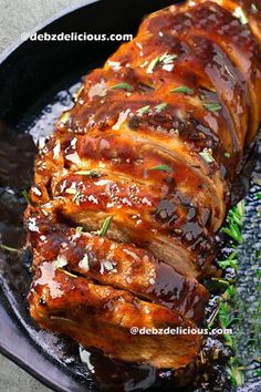 meat covered in sauce and garnished with parsley on a black platter