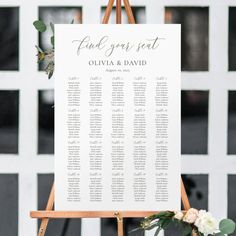 a wooden easer with seating cards on it and flowers in front of the sign