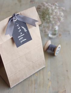 a brown paper bag with a tag on it and a flower in a vase next to it