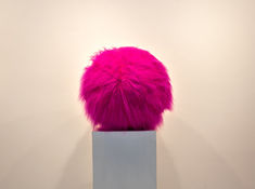 a pink furry ball sitting on top of a white pedestal in front of a wall