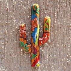 a colorful painted cactus on the side of a stone wall in front of a stucco wall