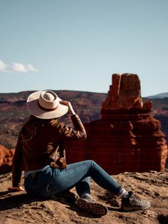 a woman sitting on top of a mountain wearing a hat