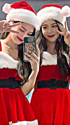 two girls dressed in santa claus outfits are looking at their cell phones