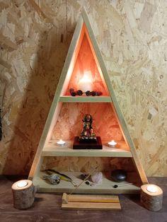 a triangle shaped shelf with candles and other items on it in front of a wall