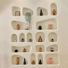 several shelves with vases and plants on them in a white walled room, all lined up against the wall