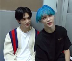 two young men sitting next to each other in front of a wall with blue hair