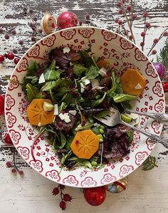 a white and red bowl filled with salad on top of a wooden table next to christmas decorations