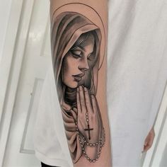 a woman's arm with a rosary and praying hands tattoo on her left upper arm