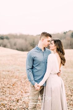 an engaged couple standing in the middle of a field