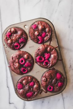 chocolate muffins with raspberries in a pan on a marble counter top