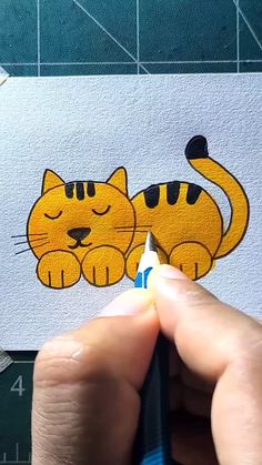 a person holding a pencil in their left hand and drawing a cartoon cat on paper