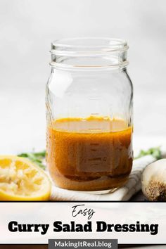 a glass jar filled with curry salad dressing next to sliced lemons and parsley