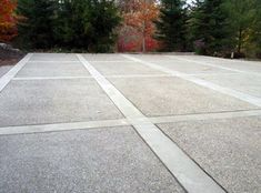 an empty concrete parking lot with trees in the backgroung and leaves on the ground