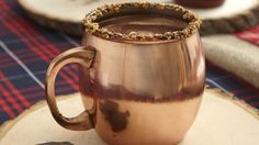 a copper mug filled with hot chocolate sitting on top of a wooden table next to some cinnamon sticks