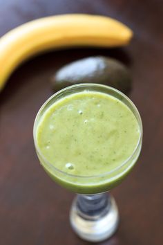 a green smoothie in a glass with a banana and avocado on the side