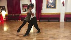 two people are dancing in a large room with red drapes on the walls and wooden floors