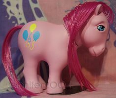 a toy pony with pink hair and blue eyes sitting on a purple cloth covered surface