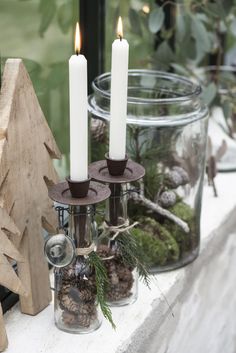 two candles sitting on top of a window sill next to pine cones and other decorations