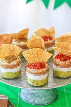 small cups filled with salsa and tortilla chips on a silver platter next to green table cloth