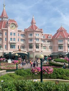 people are walking around in front of a pink building with many windows and lots of greenery