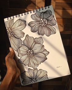 a person is holding up a notebook with flowers drawn on it and in front of them