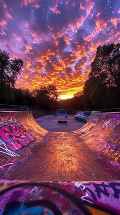 a skateboard park with graffiti on the ground and trees in the background at sunset