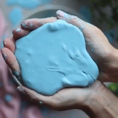 two hands are holding something blue in front of a wall with graffiti on the walls