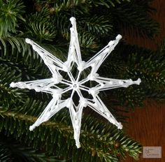 a white snowflake ornament hanging from a christmas tree