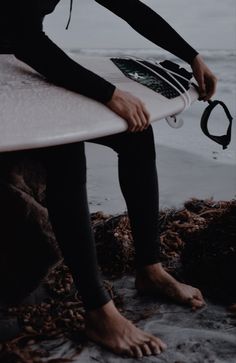 a person sitting on the beach holding a surfboard