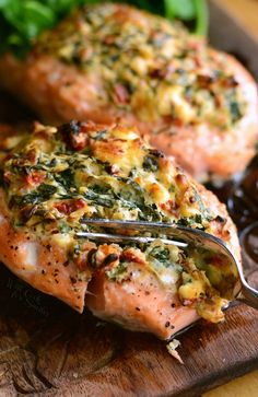 a piece of salmon with spinach and cheese on it being held by a fork