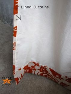 a white curtain with an orange and white flower design on it, next to a wall