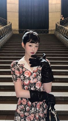 a woman standing in front of some stairs wearing gloves and holding a handbag with both hands