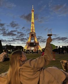 a woman laying on the ground with a glass of wine in front of the eiffel tower