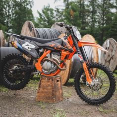 an orange and black dirt bike parked in front of some large wooden barrels on the ground