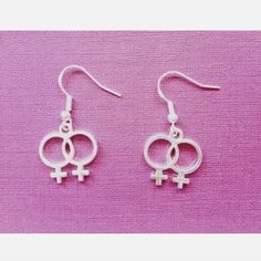 two silver earrings with symbols hanging from them on a pink background, the one in the middle