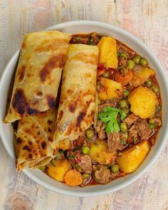 a white bowl filled with meat and veggies next to some pita bread