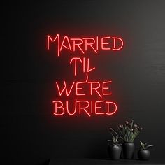 a neon sign that says married til we're buried next to two vases with flowers