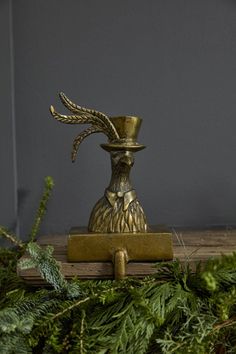 a gold vase with a feather on it sitting on top of a wooden table next to greenery