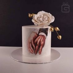 a white cake with two hands and a rose on top is sitting on a plate