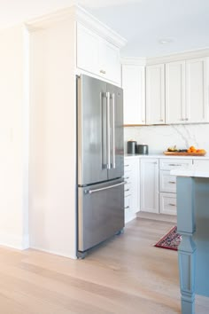 a large stainless steel refrigerator in a white kitchen with wood flooring and cabinetry