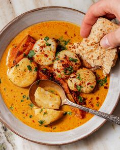 a bowl filled with soup and dumplings on top of a table next to a hand holding a spoon