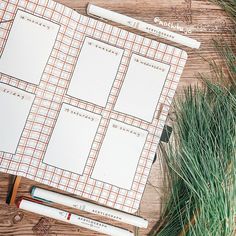 an open planner sitting on top of a wooden table next to green plants and pencils