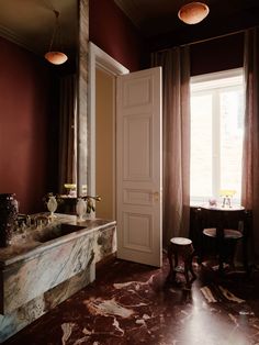 a bathroom with marble counter tops and red walls, along with an open door leading to the outside