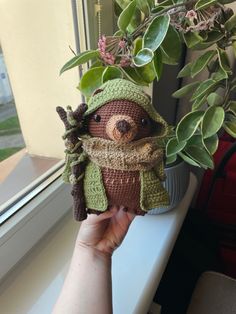 a hand holding a small stuffed animal next to a window sill with plants in it