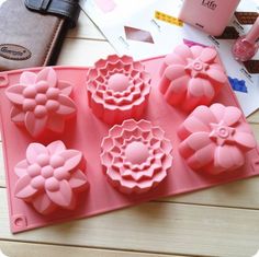 four pink flower shaped chocolate molds sitting on top of a table next to a wallet